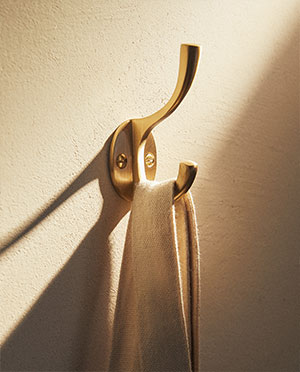 Golden light paints textured wall. Brass hook holds cream fabric strap