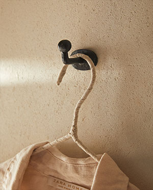 Textured beige wall with black hook holding Zara Home garment