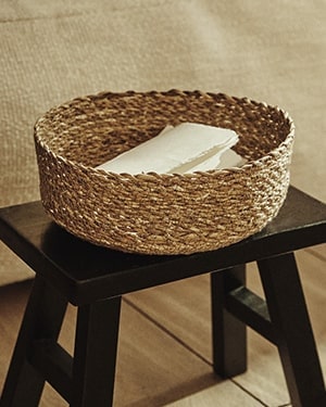 Woven basket filled with books (black stool, beige background)